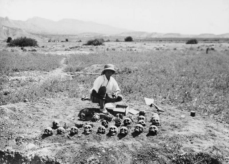 John Lindros crouching among human skulls laid out beside an excavated opening at Ayios Iakovos