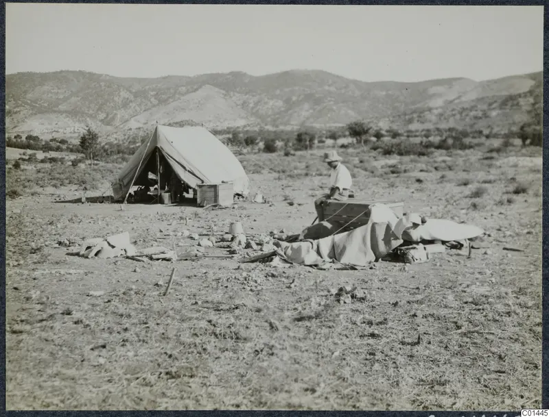 Erik Sjöqvist seated beside a wind-blown tent on dry ground, with hills behind, at Ayios Iakovos