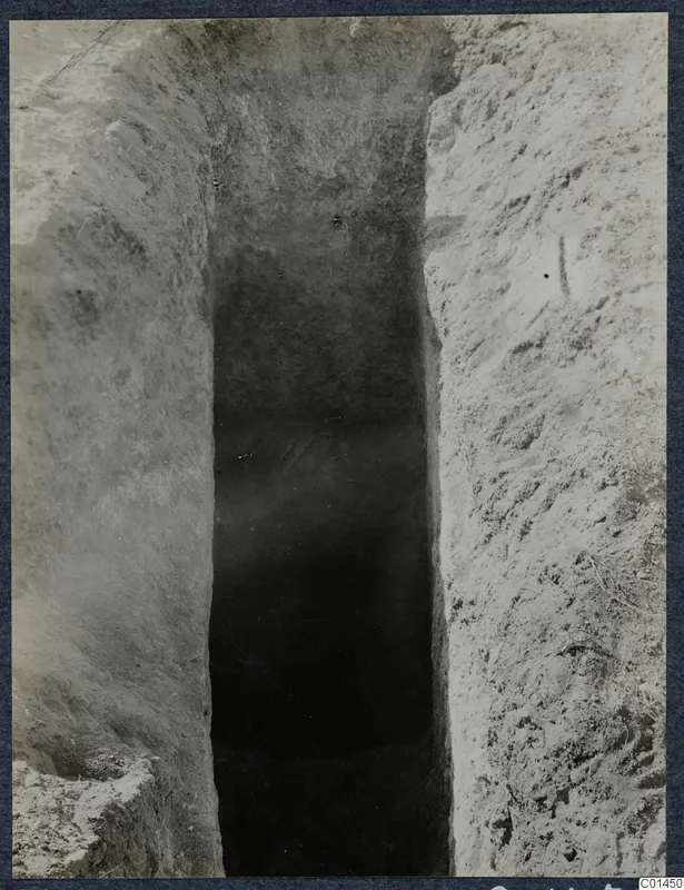 Narrow cut in excavated soil leading down to a dark opening, Tomb 12 at Ayios Iakovos during excavation