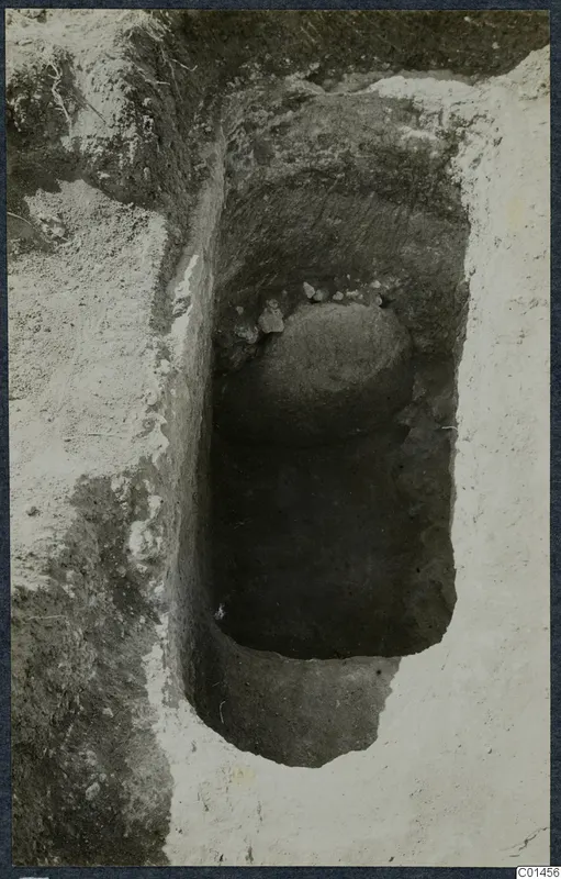 Excavated tomb at Ayios Iakovos: a rounded stone and small stones sit in a narrow cut in the soil.