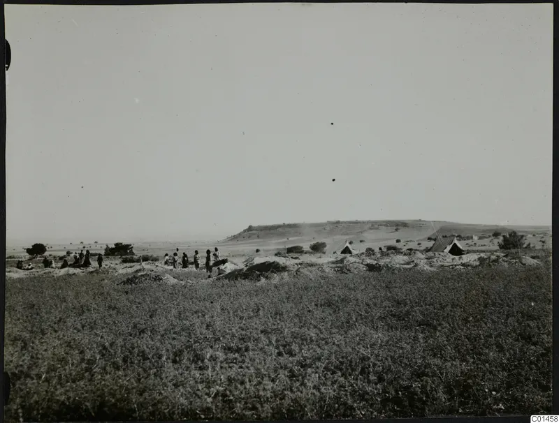 People and pointed tents on open ground at Ayios Iakovos, with a long low hill behind.