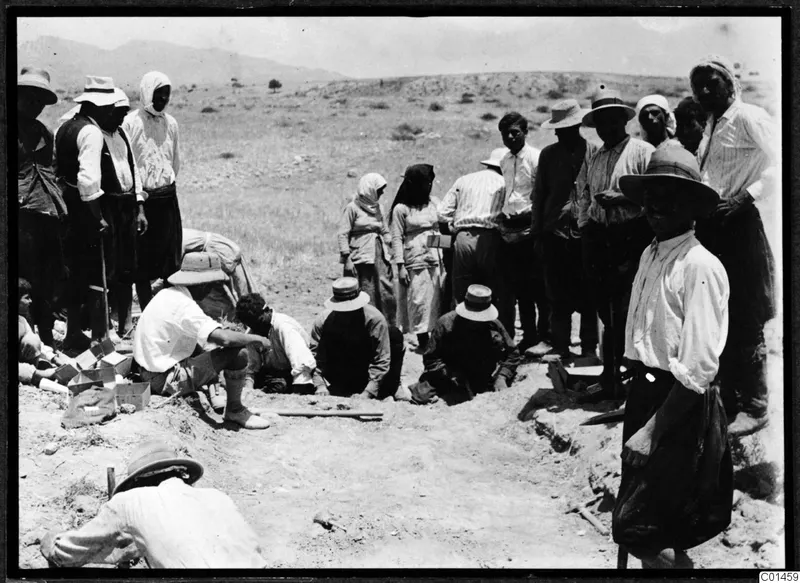 Excavation at Ayios Iakovos with a crowd of people in hats and headscarves working and standing around a shallow trench