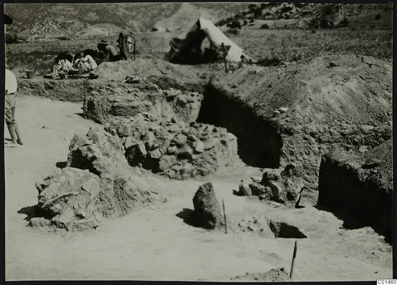 Excavation at Ayios Iakovos with stone walls exposed, a tent and a group of people in the background