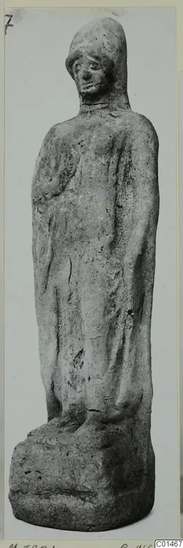 Standing figurine of a robed figure with a hooded head, photographed against a plain grey background