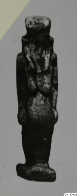 Small standing figure from Marion Tomb 50, dark with pale speckled patches, shown against a plain grey backdrop.