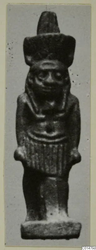 Small dark figurine named Nefertum, with a tall headdress, standing on a flat rectangular base.