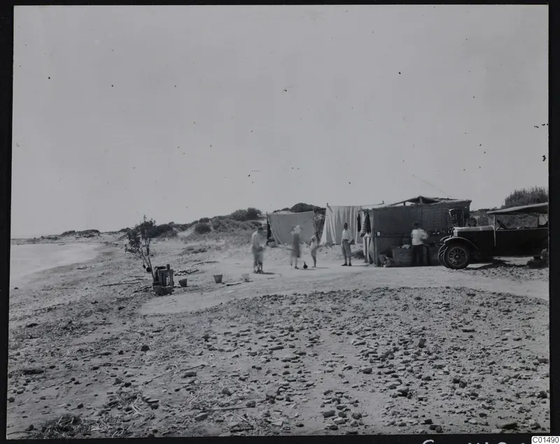 Camp on a stony beach at Oura with people, a child, canvas-screened shelters and an open car.