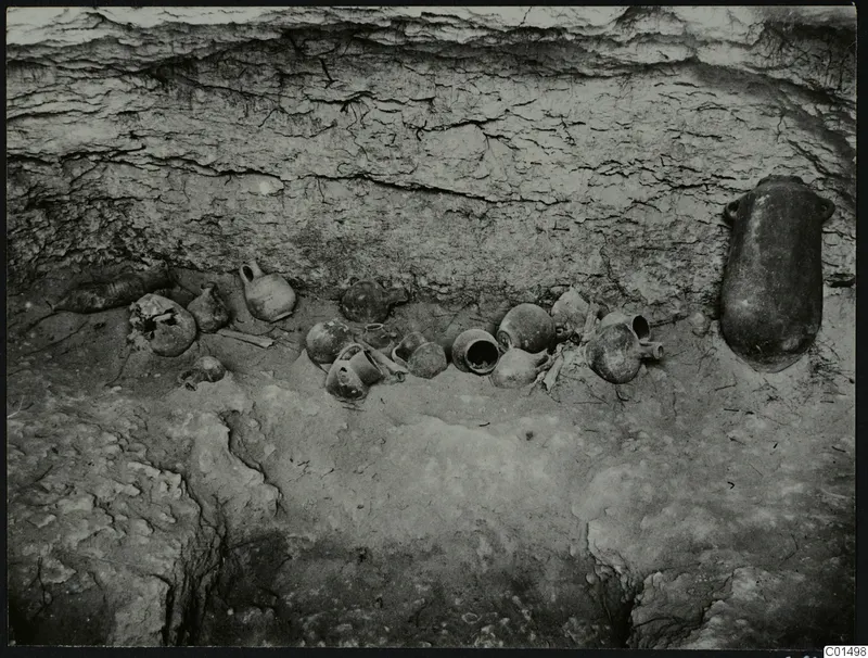 Pottery vessels lying in situ on the floor of an excavated cutting, with a large jar standing against the cut wall