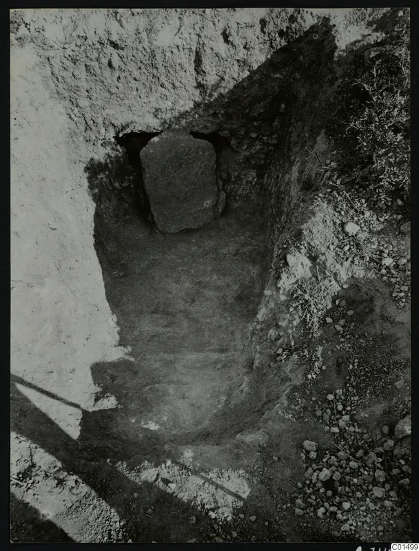 Excavation cutting at Kountoura Trachonia with a large upright stone slab set in a dark recess at the back