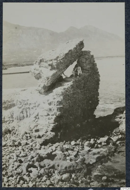 Man sitting in the shadow beneath a large overhanging stone block by the sea at Lambousa