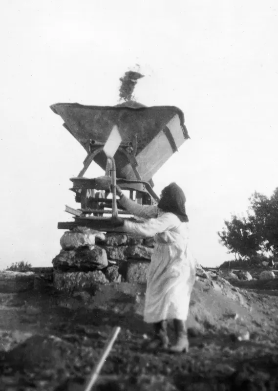 Praxou working at a hopper-like machine on a stone base at Vouni, earth spilling from its top