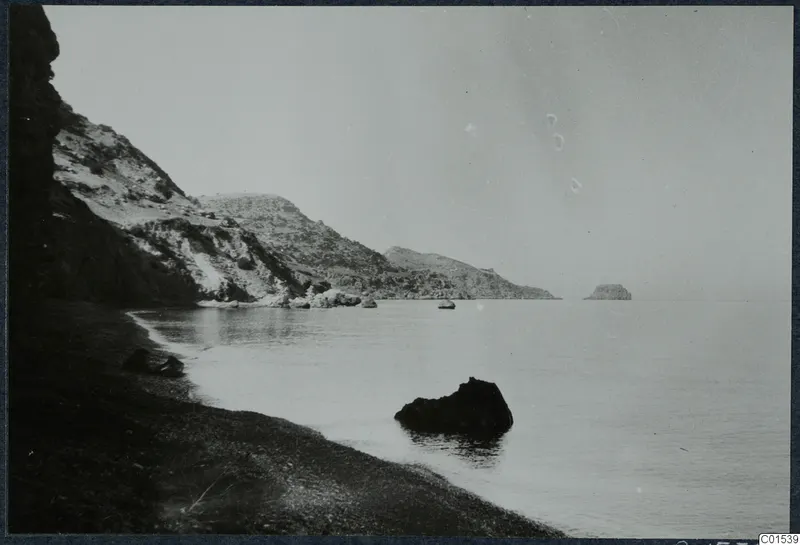 Rocky shoreline with a dark pebble beach, calm sea and a cliff at left, near Vouni.