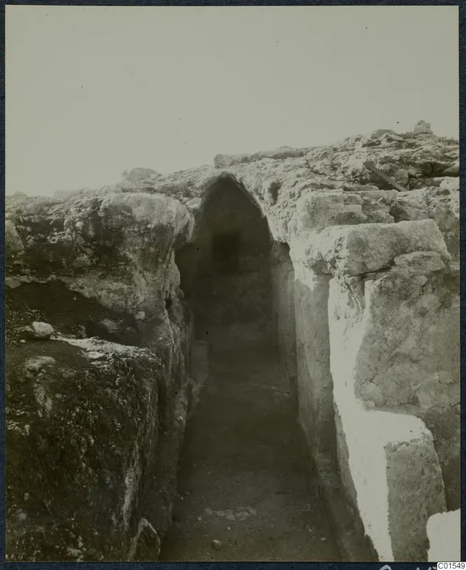 Excavated passage between rough stone walls, with an arched opening at the far end, at the Vouni palace
