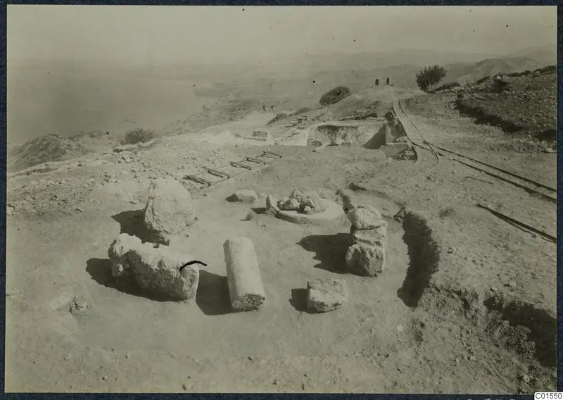 Finds in situ at Vouni with stone blocks, a column drum and a ladder-like frame on a hilltop above the sea.