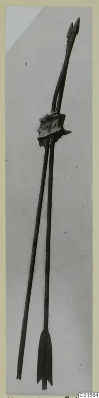Two long metal arrows bound together by a corroded lump of metal, photographed against a plain grey background.