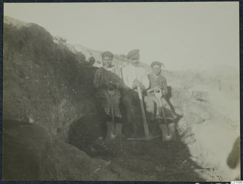 Solon and two workers sitting in an excavation trench, holding spades and a pick