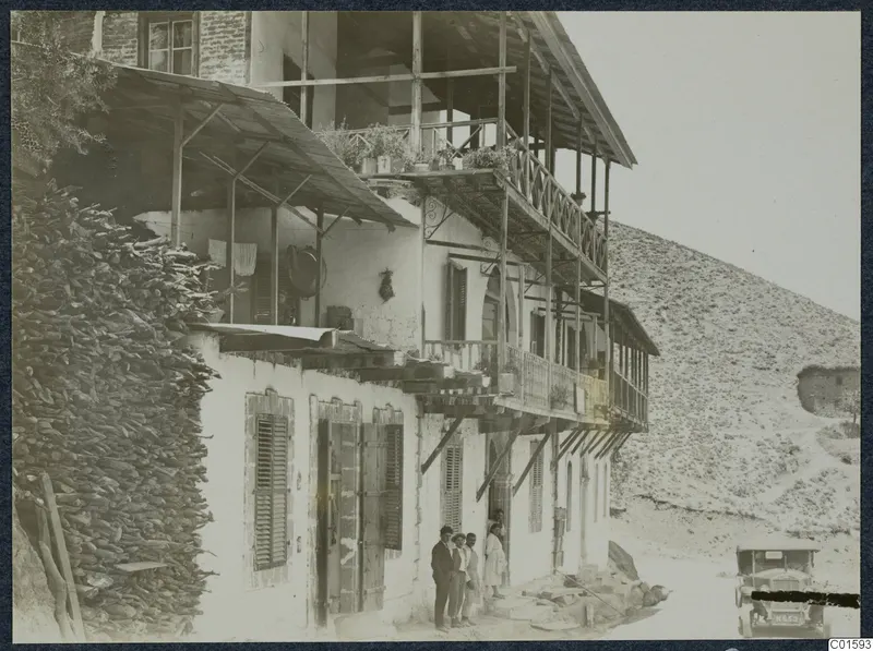 Two-storey house with timber balconies and shuttered windows in Kalopanayotis village, with people standing at the doorway.