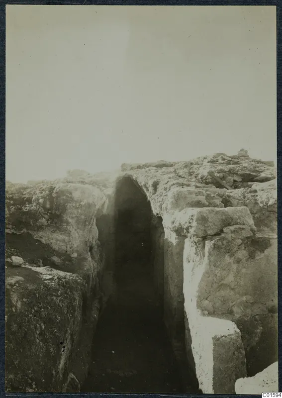 Excavated trench between cut stone walls at Vouni Palace, with a rounded opening in the far wall