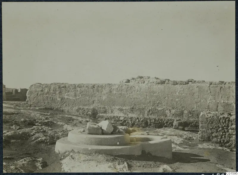 Long weathered wall at Vouni Palace with a circular stone base and broken stone blocks in the foreground