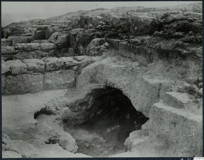 Excavation at Vouni palace showing rough stone walls and an arched rock-cut opening leading down into a dark hollow