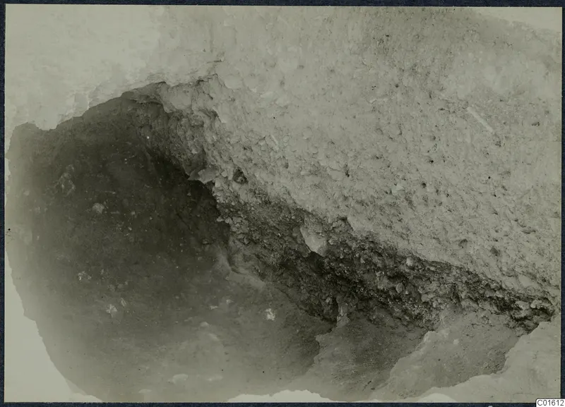 Close view of an excavation cutting at the palace at Vouni, with a pale hard surface above a dark hollow and layered soil.