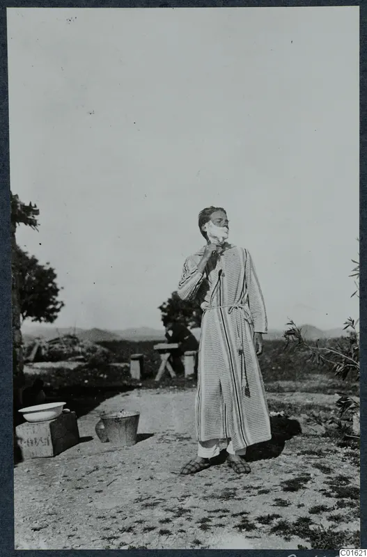 Alfred Westholm shaving outdoors at Vouni, wearing a striped housecoat with lather on his face.