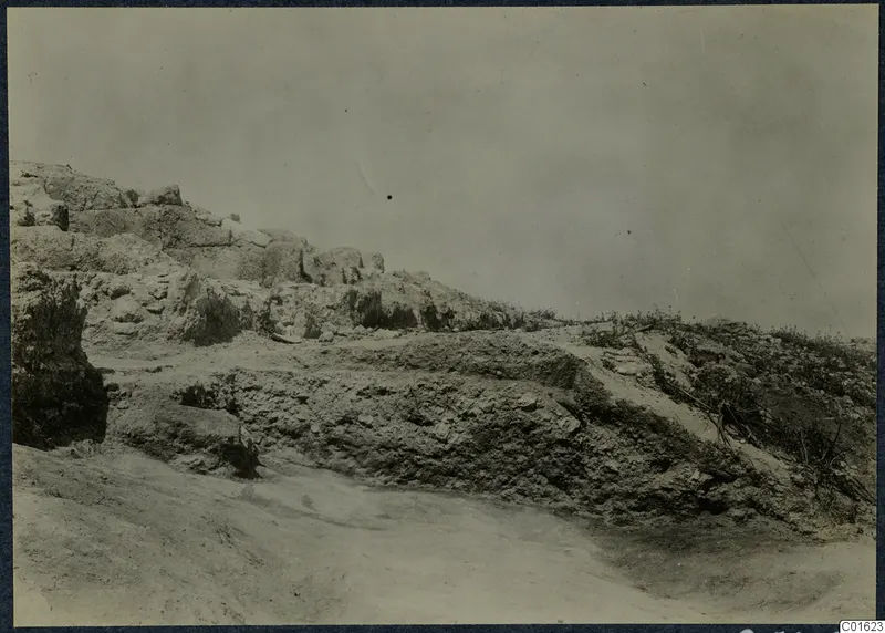 Ruined stone wall and rubble on a dry slope at the palace at Vouni, with grass growing along the top