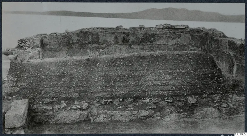 Ruined wall with layered pebbly fill and stones at the base, at the palace at Vouni, with hills behind