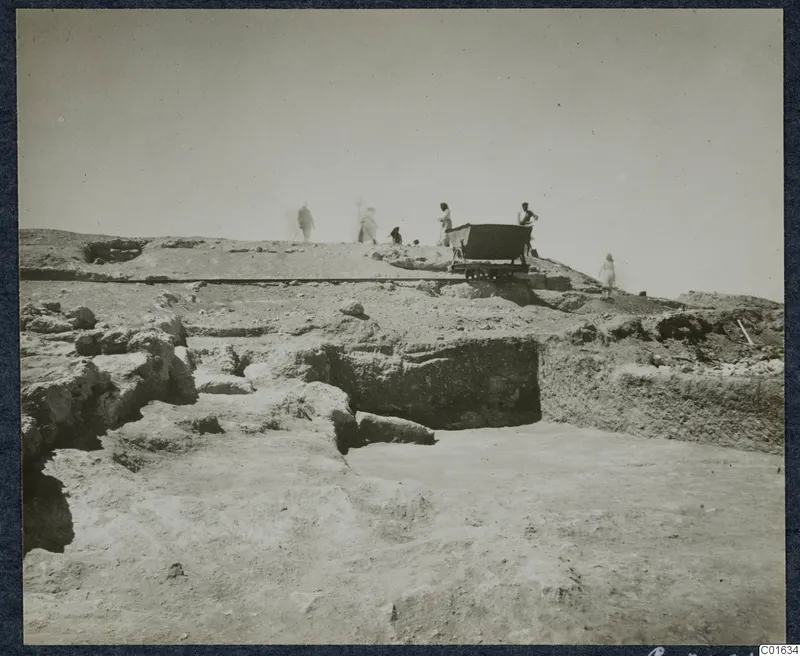 Excavated stone walls at Vouni palace, with a rail cart and several blurred figures on the ridge behind.
