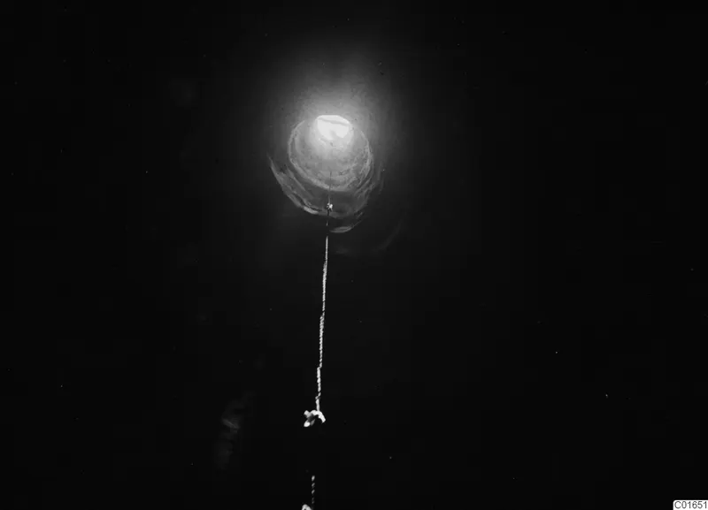 Dark view of a shaft or pit with a bright light at its mouth and a string hanging down the middle