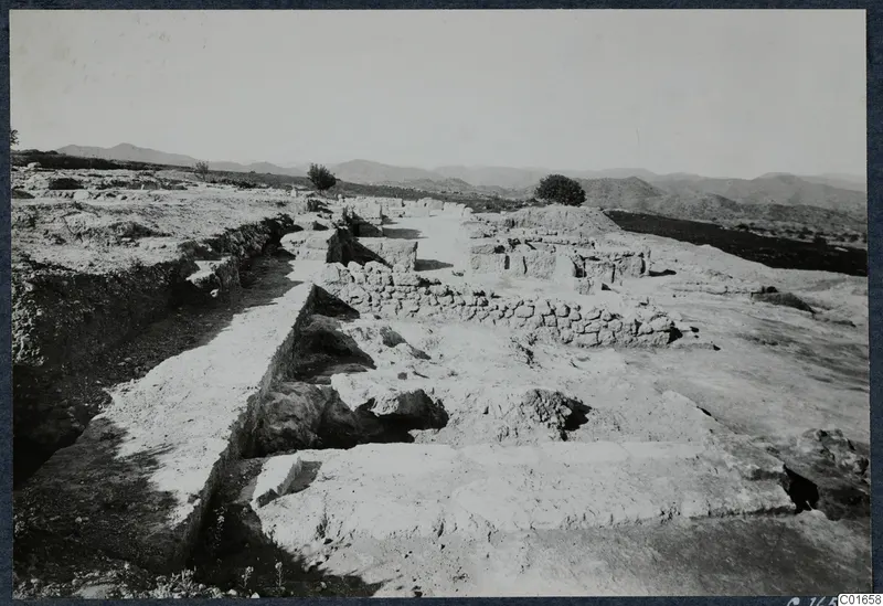 Excavated area at Vouni Palace with low stone walls, a cut rock edge and a trench, with hills behind