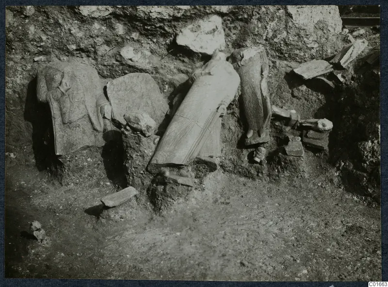 Stone sculptures and architectural fragments lying in excavated soil against a rock face at Vouni Palace.