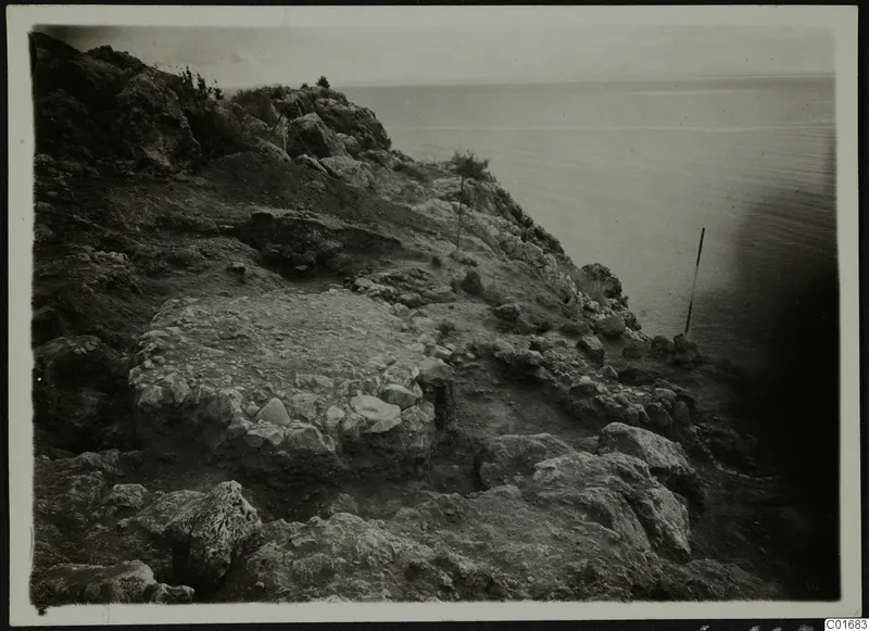Excavated rocky slope at Petra tou Limniti with exposed stone walls running down toward the sea.
