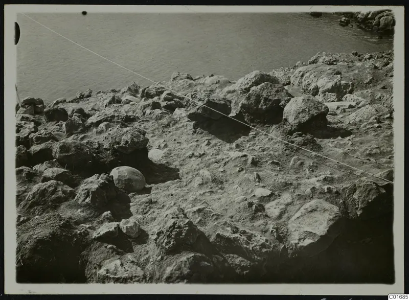 Rocky shoreline at Petra tou Limniti with boulders in the foreground and calm water beyond.