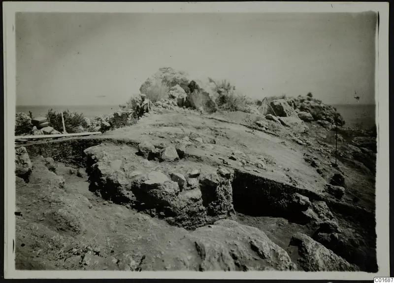 Excavation at Petra tou Limniti with a man seated among stones above the sea