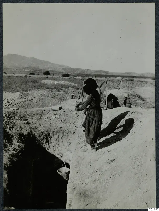 Woman at the edge of a trench at Ayios Iakovos, lowering a bucket on a rope into the excavation