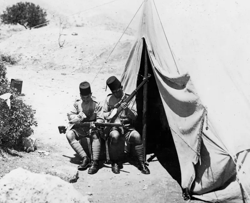 Two saptiena seated outside a tent at Vouni, each handling a rifle