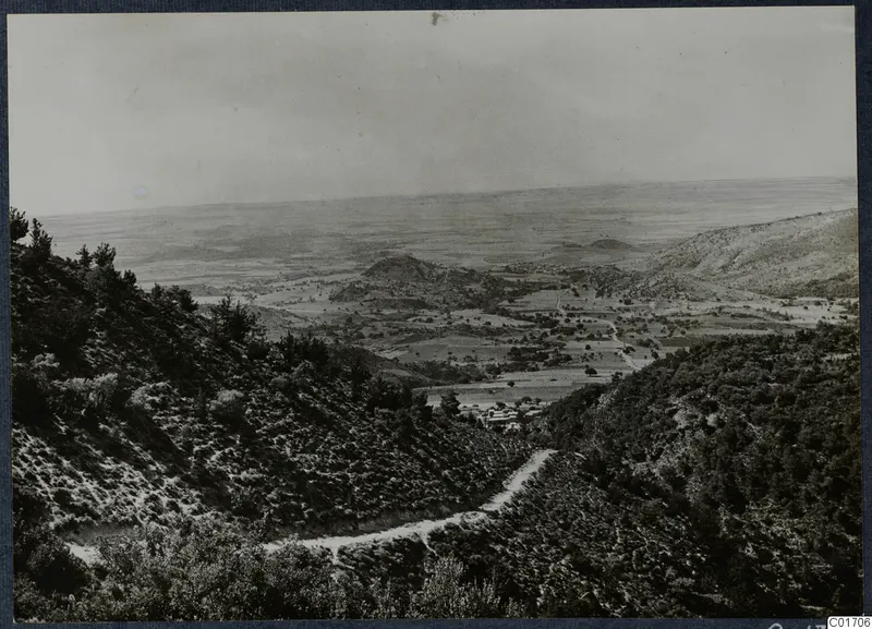 View over a valley with fields and a village, from a wooded mountainside with a winding road, Troodos and Machairas area