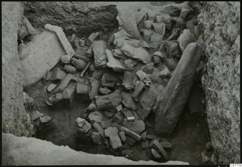 Overview of a pit crowded with broken stone statues and blocks at Kition, with several heads visible at the upper right