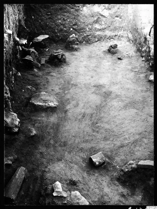 Excavated room at Kition with stone blocks and rubble scattered over an earth floor, walls along two sides