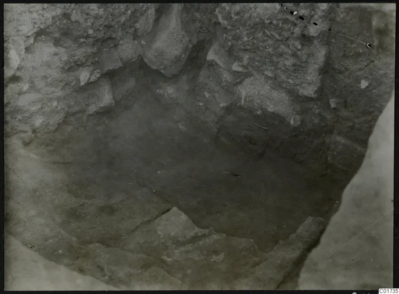 Excavation pit at Kition seen from above, with cut soil walls and stones on the floor.