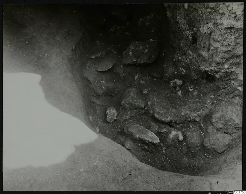 Excavated corner at Kition with stones set in dark soil against a pale rock face