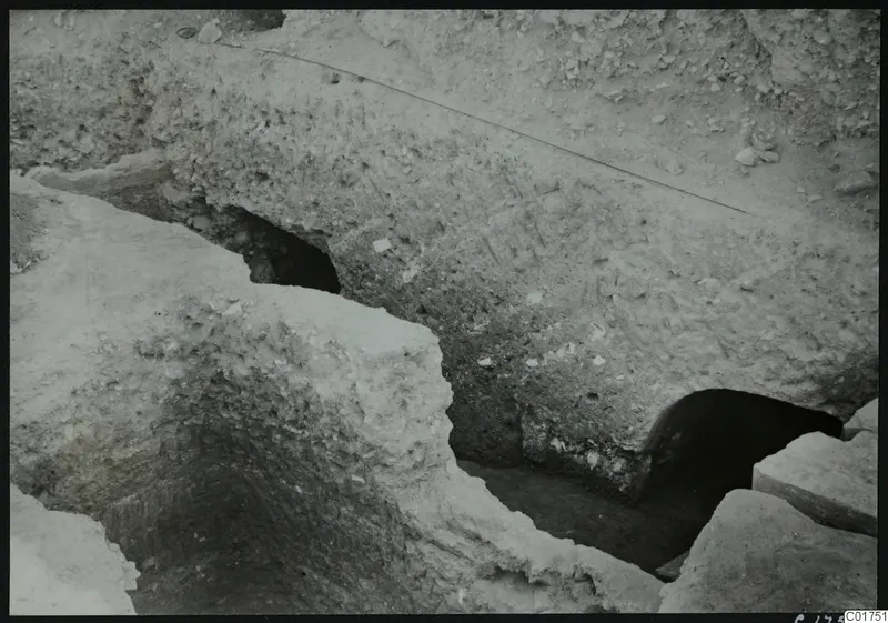 Excavated profile at Kition with dark openings at the base of a pale earth face, leading to galleries