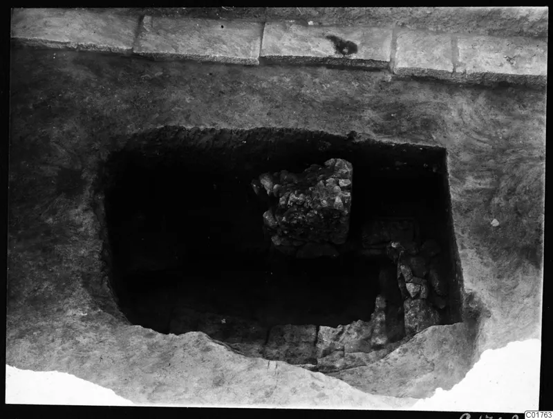 Excavated central pit at Kition, seen from the north, with a block of rubble stones and stone courses inside.