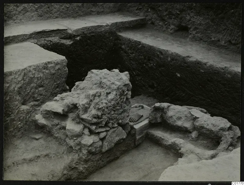 Excavation trench at Kition with rubble stone masses, a stepped ledge, and a flat slab holding a small object