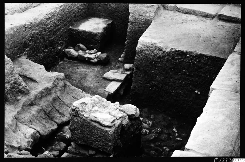 Excavation trench at Kition below the cult room, with stone walls, flat slabs and a square stone block in the foreground.