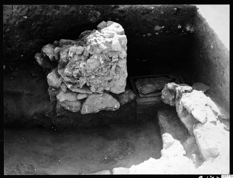 Excavation trench at Kition with a large heap of limestone blocks and a dark stone object in a shallow cut