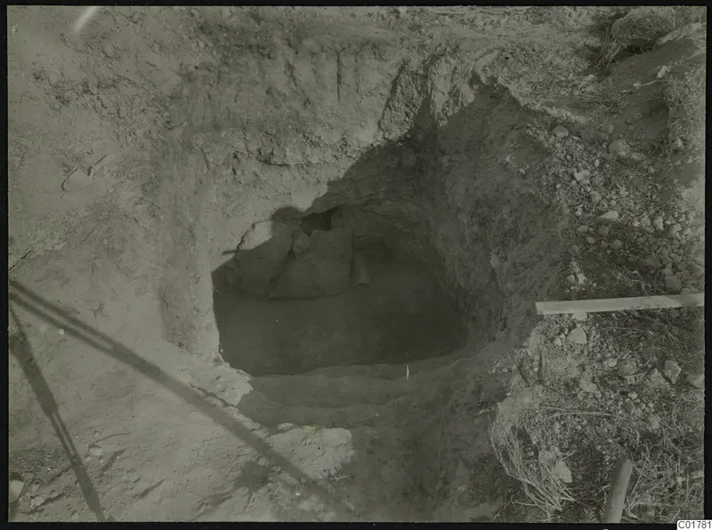 Excavated cut at Kountoura Trachonia with stones at the back of a dark hollow and a plank lying at the right edge