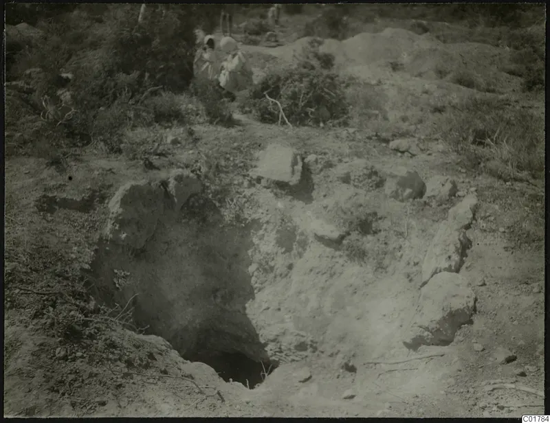Excavation pit with loose stones and two people among bushes at Kountoura Trachonia