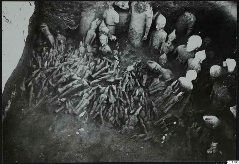 Excavation at Ayia Irini showing many figurines and sculpture fragments lying in situ in a trench.